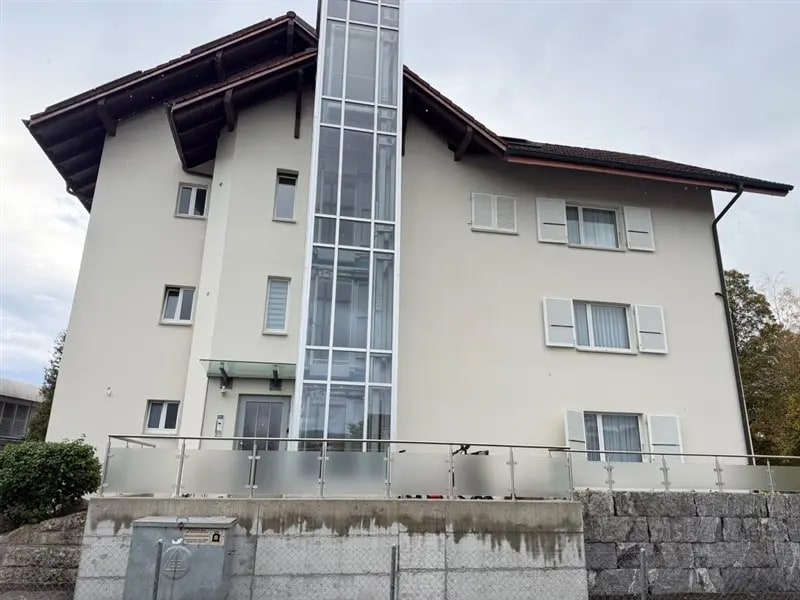 Mehrfamilienhaus mit fertiger heller Fassade, Glasliftturm und weissen Fensterläden