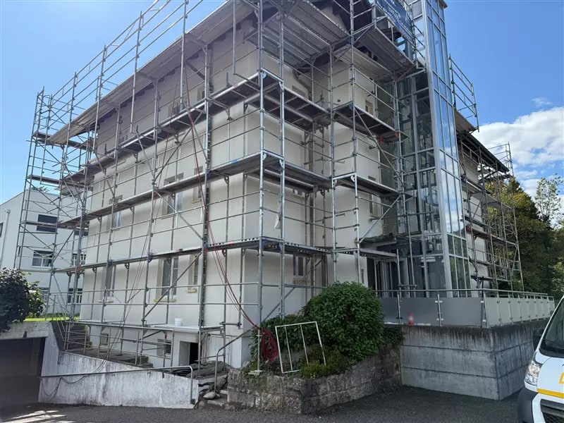 Mehrfamilienhaus mit Glasliftturm während der Fassadenarbeiten, eingerüstet