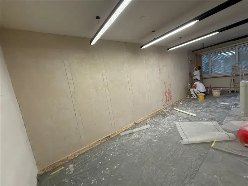 Zwei Mitarbeiter in weisser Arbeitskleidung arbeiten in einem Raum mit abgedecktem Boden an einer langen Wand