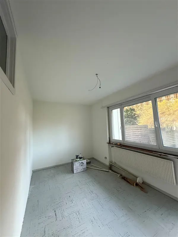 Leerer Raum mit hellen, weissen Wänden und Decke, einem Fenster mit Heizkörper und gemustertem Boden