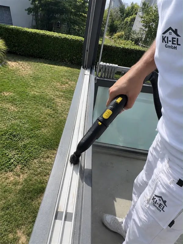 Mitarbeiter in KI-EL-Arbeitskleidung reinigt einen Fensterrahmen mit einem Dampfreiniger