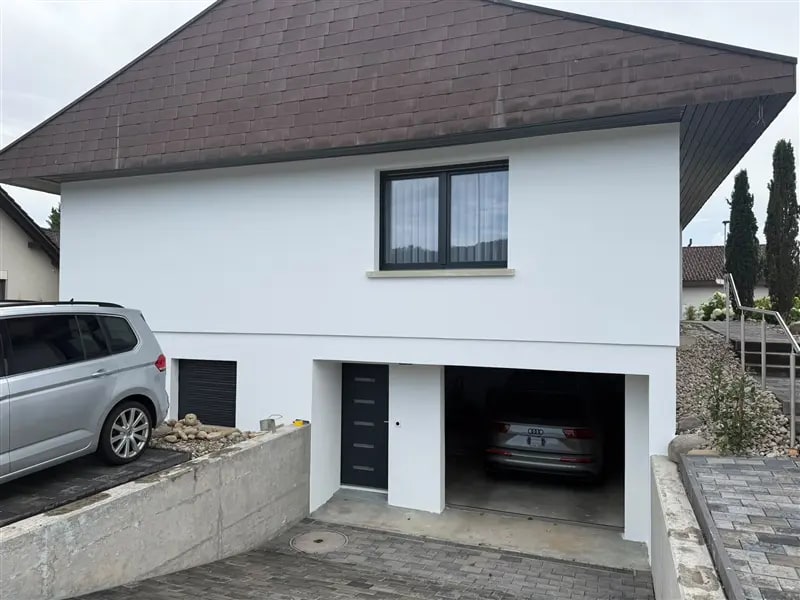 Weiss verputztes Einfamilienhaus mit braunem Dach und Garage