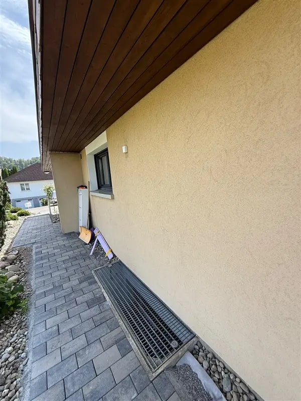 Gelb verputzte Hausfassade mit Holzuntersicht und gepflastertem Weg